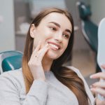 Photo of a girl in a dentist&#39;s chair examining her teeth in the mirror after professional oral hygiene