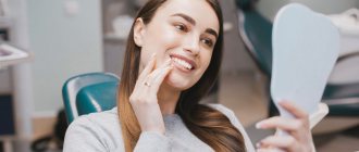 Фото девушки в кресле стоматолога, которая рассматривает свои зубы в зеркале, после профессиональной гигиены полости рта